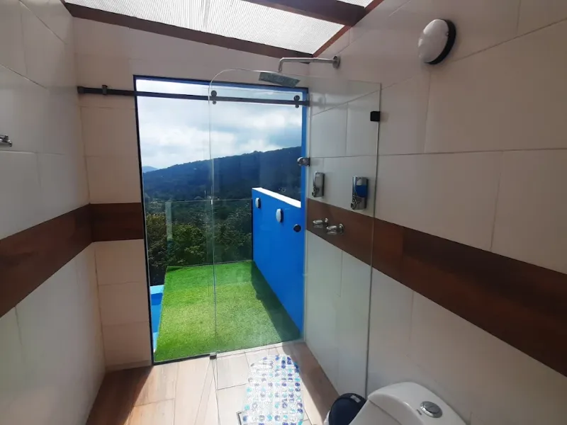 Baño con ducha de vidrio que abre hacia jardín privado con grama y vista a las montañas, techo con tragaluz