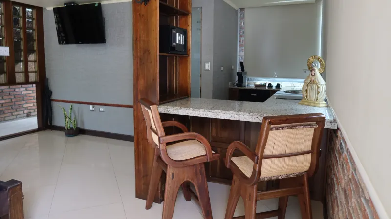 Cocina americana con barra de granito, dos sillas altas de madera y mimbre, microondas empotrado y televisor en pared