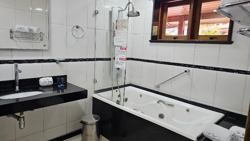 Baño en blanco y negro con tina de hidromasaje, ducha de vidrio, lavamanos con mesón negro y ventana de madera