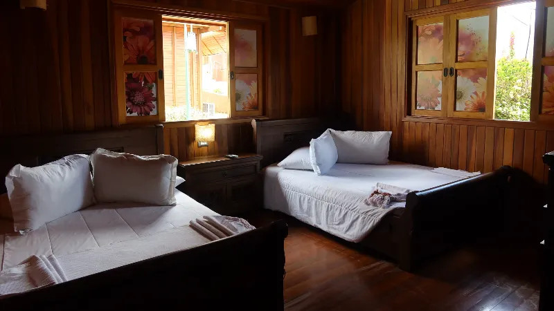 Habitación con dos camas individuales de madera, ventanas con láminas decorativas de flores rosas y piso de madera oscura