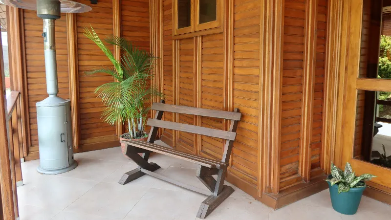 Terraza de cabaña con banca de madera, planta de palma, calefactor de exterior y fachada de tablones de madera