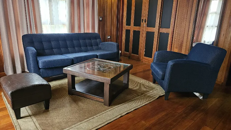 Sala con sofá y sillón azul marino, mesa de centro con vidrio, puf oscuro y tapete sobre piso de madera en cabaña rústica