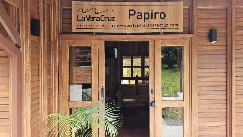 Entrada principal de la cabaña Papiro de La Vera Cruz en Bailadores, Mérida, con fachada y puerta de madera y jardín al fondo