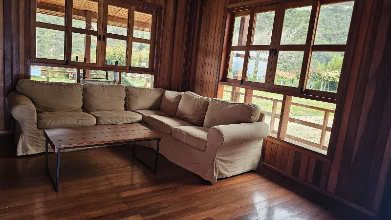 Sala luminosa con sofá esquinero beige, mesa de centro metálica y amplias ventanas con vista al jardín y montañas