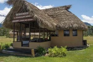 Entrada del Campamento Uruyen con churuata de techo de palma, letrero de bienvenida y porche con sofás, rodeada de vegetación y cielo azul.