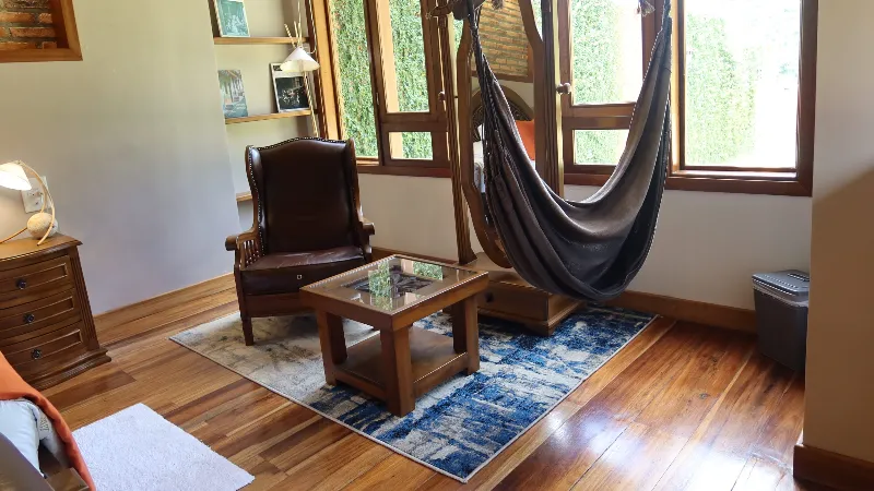 Zona de estar con sillón de cuero, mesa de centro con vidrio, tapete azul, hamaca colgante y ventanas con vista al jardín