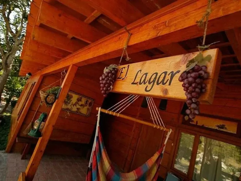 Letrero de madera con el nombre "El Lagar" decorado con racimos de uvas, colgado en el porche de madera junto a una hamaca colorida.