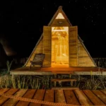 Cabaña A-frame iluminada por dentro durante la noche estrellada en el glamping Cubagua Lodge, isla de Cubagua, Nueva Esparta, Venezuela