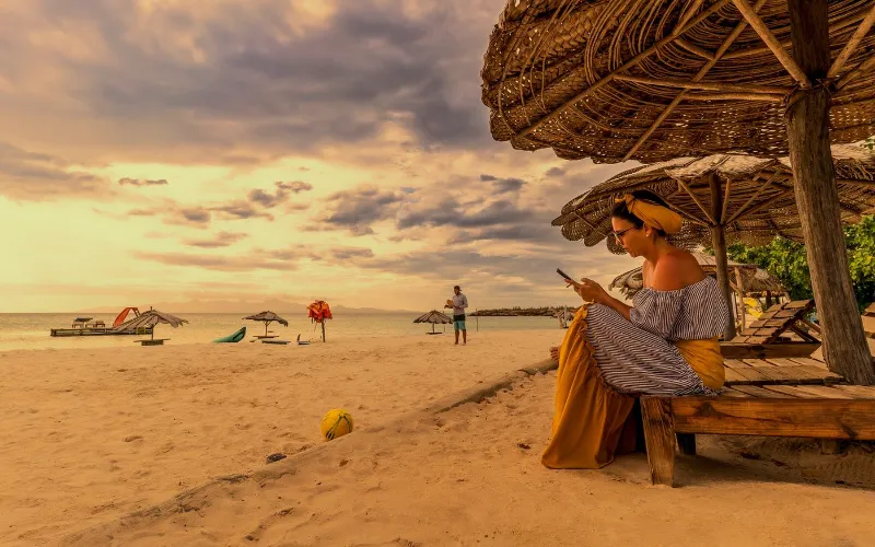 Mujer descansando bajo sombrilla de palma al atardecer en la playa de la isla de Cubagua, Nueva Esparta, Venezuela, cerca del glamping Cubagua Lodge