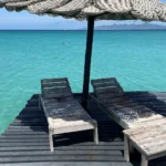 Dos tumbonas bajo sombrilla de palma sobre muelle flotante rodeado de agua turquesa en el glamping Cubagua Lodge, isla de Cubagua, Nueva Esparta, Venezuela
