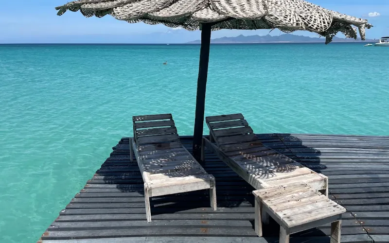 Dos tumbonas bajo sombrilla de palma sobre muelle flotante rodeado de agua turquesa en el glamping Cubagua Lodge, isla de Cubagua, Nueva Esparta, Venezuela