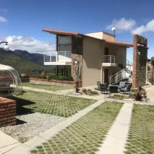 Edificio principal de la posada Rafaela y Cristóbal con jardines y burbuja de descanso, rodeado de montañas andinas en Mucuchíes, Estado Mérida, Venezuela