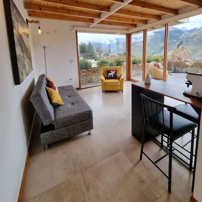 Sala de estar de cabaña de la posada Rafaela y Cristóbal con sofá, barra de desayuno y ventanales con vista a los Andes de Mucuchíes, Estado Mérida, Venezuela