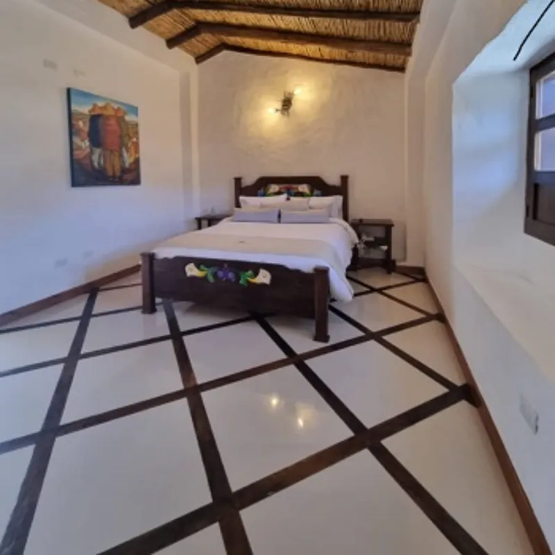 Habitación acogedora de cabaña de la posada Rafaela y Cristóbal con cama de madera tallada, techo de palma y piso de mármol en Mucuchíes, Estado Mérida, Venezuela