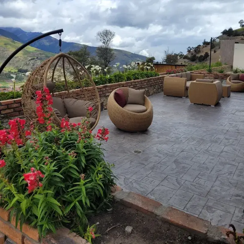 Terraza exterior con silla colgante tipo huevo, flores rojas y mobiliario de mimbre con vista a los Andes en la posada Rafaela y Cristóbal, Mucuchíes, Estado Mérida, Venezuela