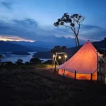 Carpa bell tent iluminada al anochecer con vista al embalse y montañas bajo cielo azul con nubes rosadas