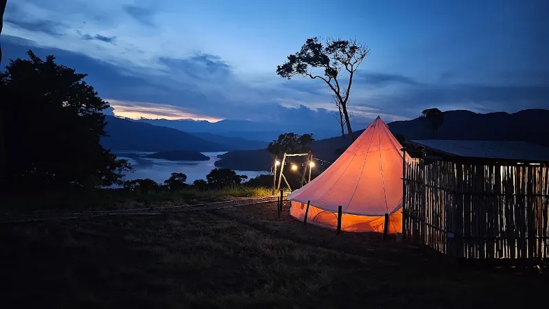 Carpa bell tent iluminada al anochecer con vista al embalse y montañas bajo cielo azul con nubes rosadas