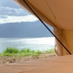 Vista desde el interior de la carpa hacia el embalse tranquilo y montañas boscosas a través de la entrada entreabierta