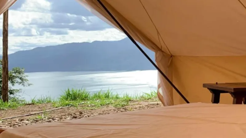 Vista desde el interior de la carpa hacia el embalse tranquilo y montañas boscosas a través de la entrada entreabierta