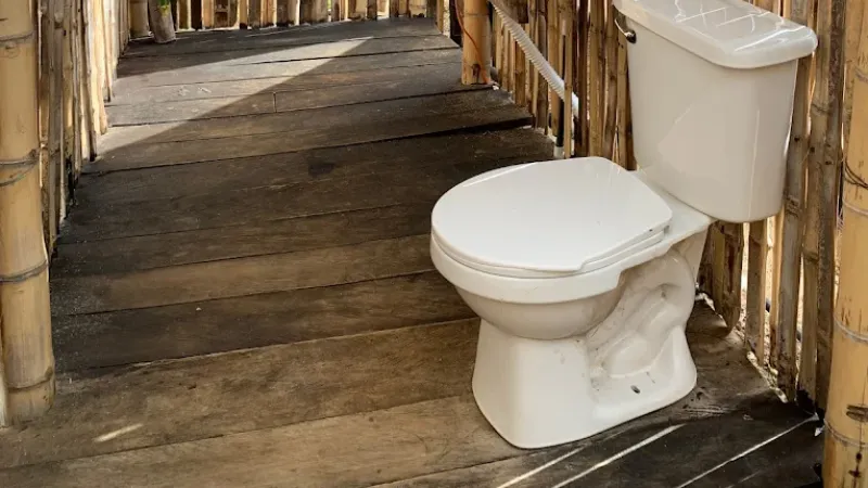 Baño rústico con sanitario blanco sobre piso de madera, rodeado de paredes de guadua en corredor al aire libre