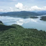 Vista aérea del embalse rodeado de colinas boscosas y reflejos de nubes en el agua bajo cielo despejado