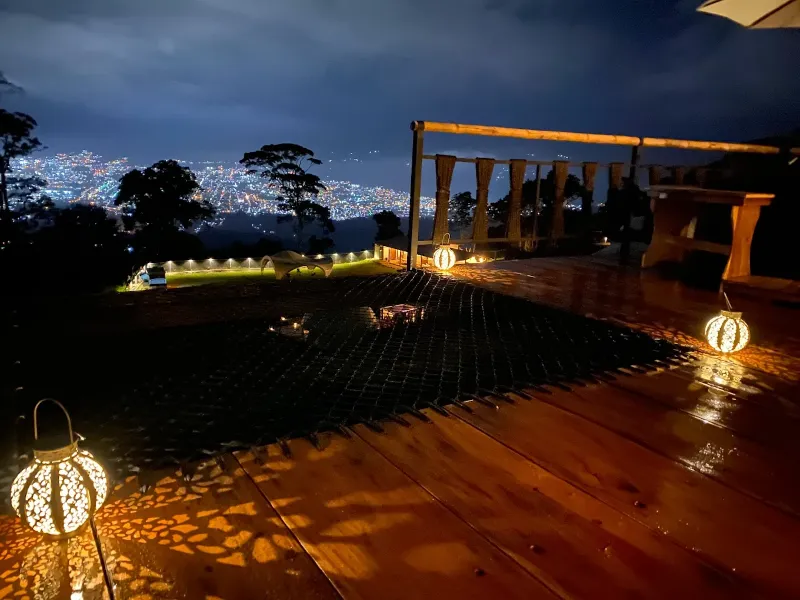 Deck nocturno iluminado con linternas decorativas, hamaca de red y vista panorámica a las luces de la ciudad entre árboles