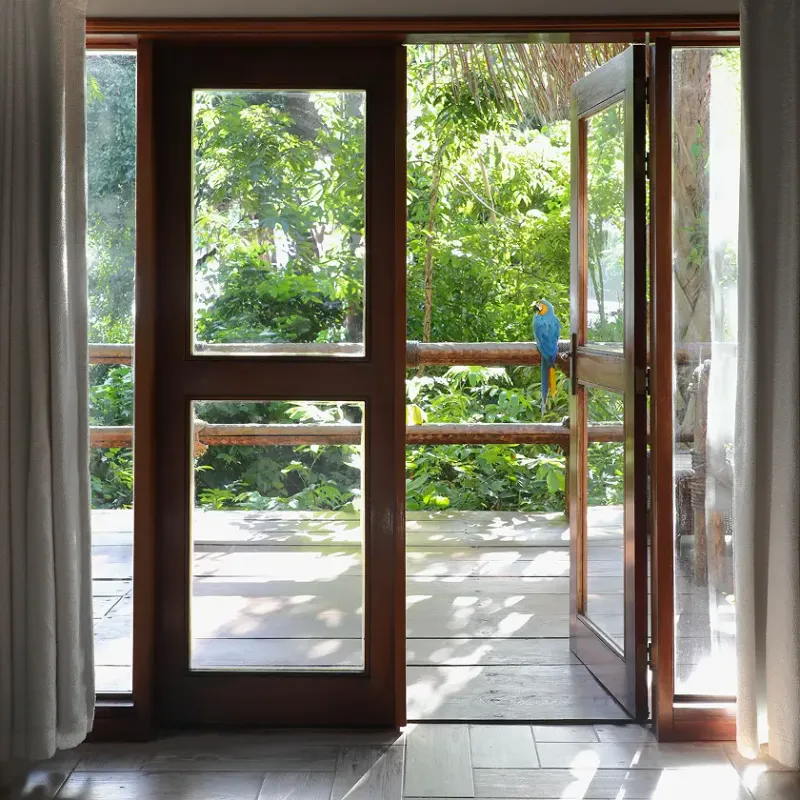 Puerta de madera con paneles de vidrio abierta hacia una terraza de madera con barandal rústico, con una guacamaya azul y amarilla posada en la puerta, rodeada de vegetación tropical exuberante en Waku Lodge, Canaima Venezuela.
